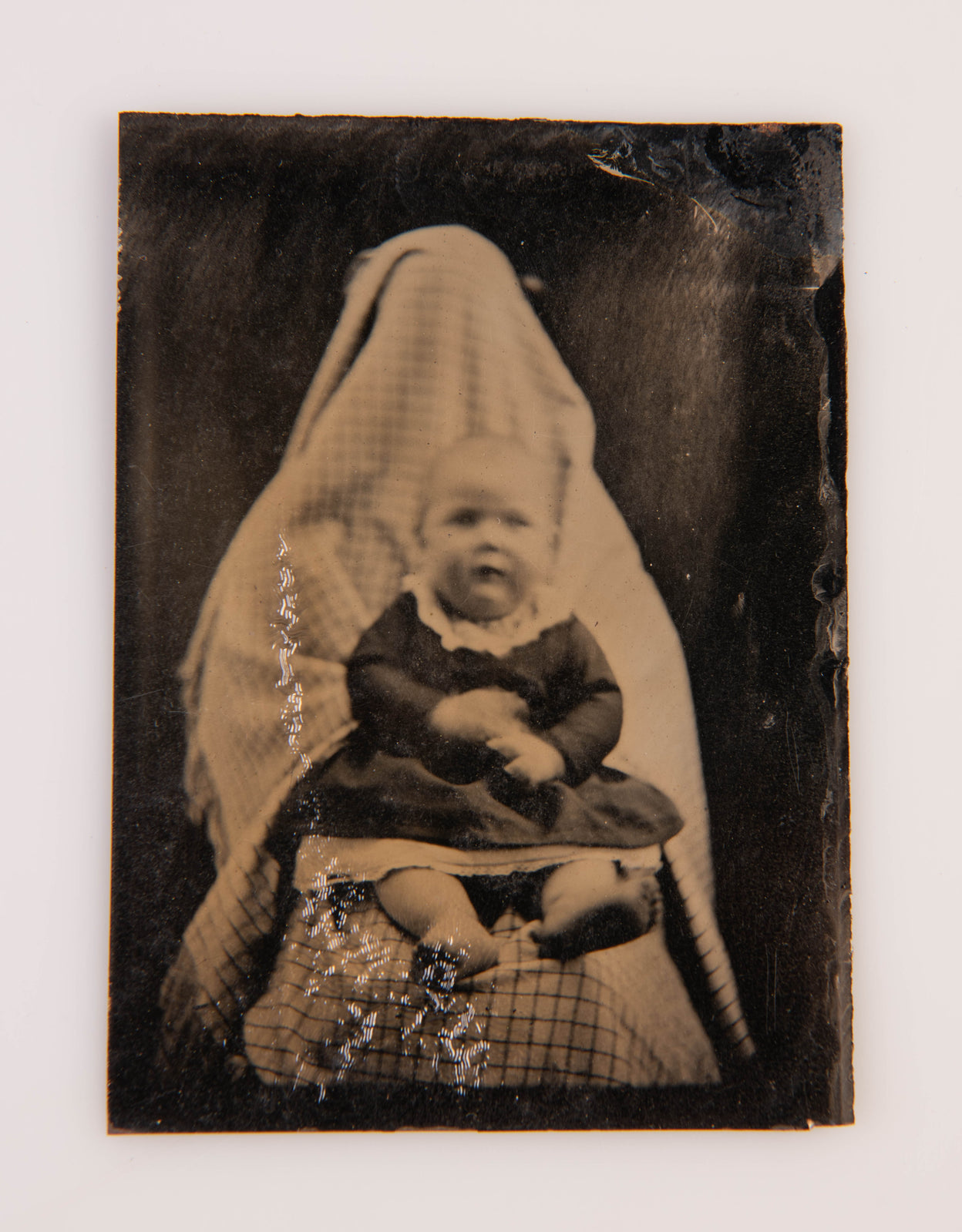 [Tintype portrait of a baby held in the lap of a person concealed by cloth].