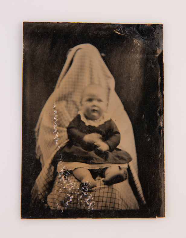 [Tintype portrait of a baby held in the lap of a person concealed by cloth].